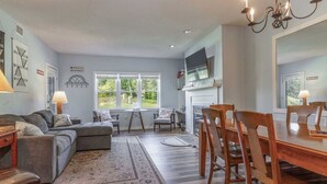 Een woonkamer met een bank, stoelen, een eettafel en een open haard.