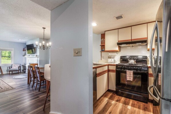 A modern kitchen with wooden cabinets, a stainless steel refrigerator, and a black stove. - Cozy Slopeside Escape - Ski-In/Out Condo at Okemo (Ludlow)