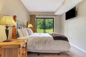 Een hotelkamer met een bed, nachtlampjes, een flatscreen televisie en uitzicht op groen.
