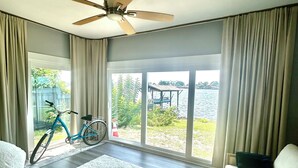 Un salón amplio con un ventanal grande, un ventilador de techo, una bicicleta y un sofá blanco.