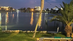 Vista al agua con una palmera, una terraza de madera y una mesa con sillas.