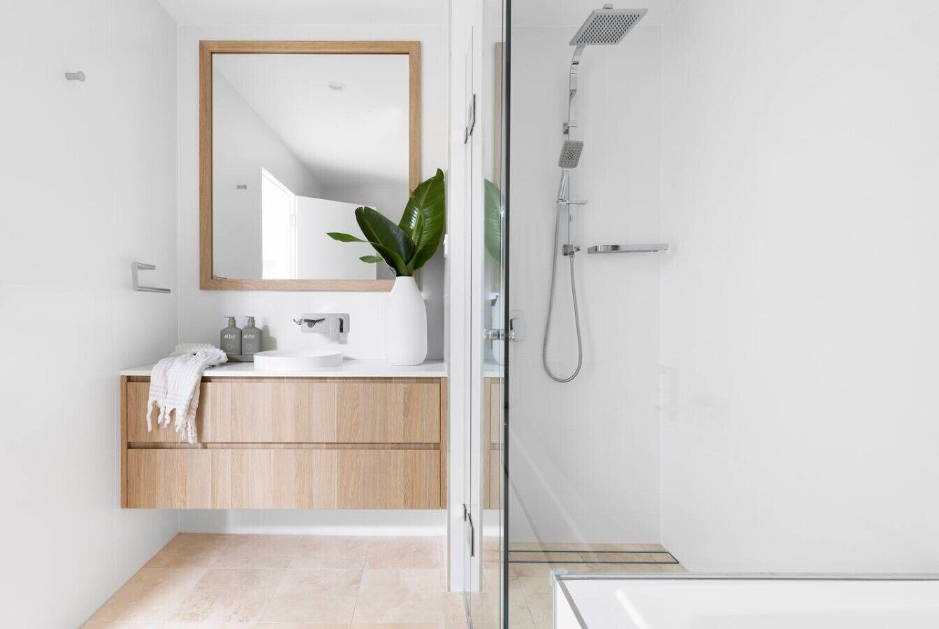 Une salle de bain moderne avec un meuble-lavabo en bois, un grand miroir, une douche et une plante en pot.