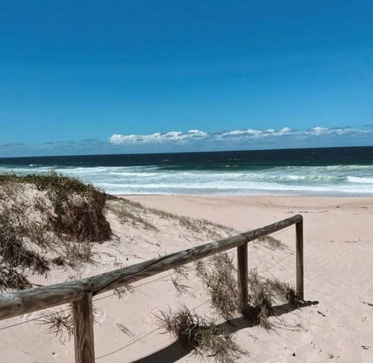 Ein Strand mit einer Holzumzäunung, Sanddünen und dem Meer.