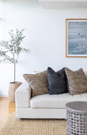 Un canapé blanc agrémenté de coussins à motifs, un pot de fleurs en osier et un tableau encadré accroché au mur.