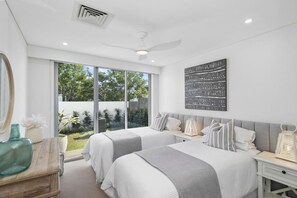 A bedroom with two beds, a large window, a ceiling fan, and a wall-mounted artwork.