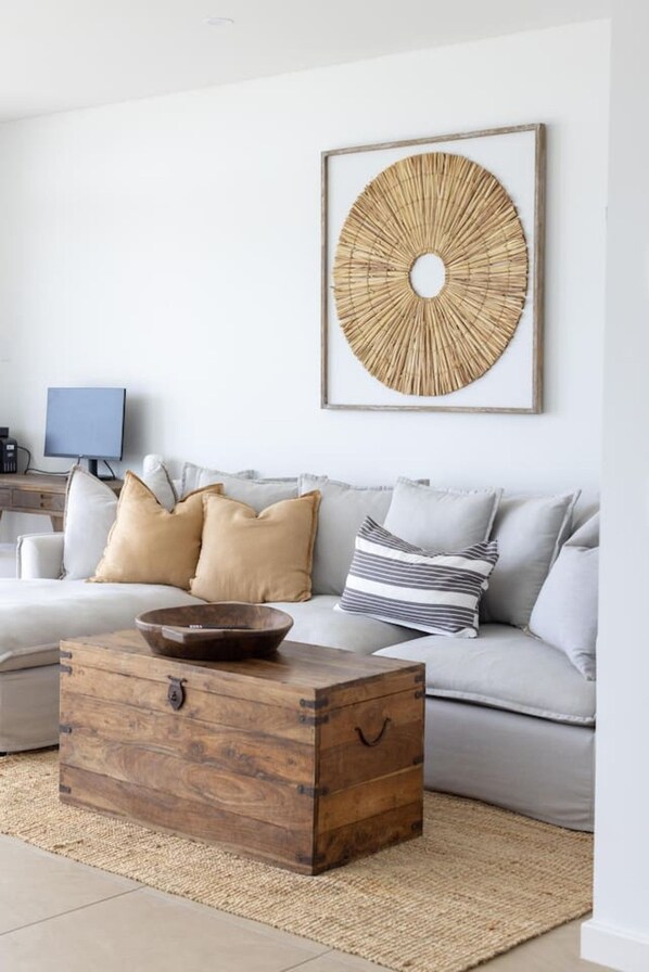A living room with a sofa, cushions, a wooden chest, a woven rug, and a wall-mounted circular artwork.