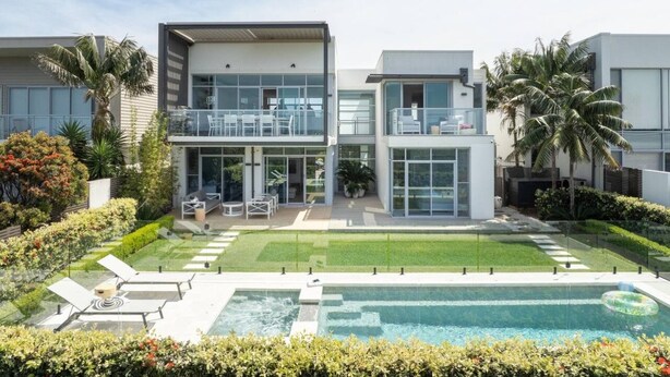 Una casa moderna de dos pisos con piscina, mobiliario exterior y jardines exuberantes.