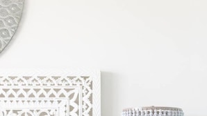 Una cama blanca con un cabecero estampado, una mesita de noche con una lámpara y un interruptor de luz en la pared.