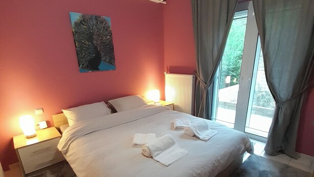 Un dormitorio con una cama, dos mesitas de noche, una lámpara de noche, un radiador y una ventana con cortinas.