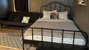 A bedroom with a bed, a sofa, a patterned rug, and artwork on the walls.