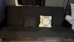 A dark-colored sofa with two cushions, one patterned and one with a floral design, and a wooden floor.