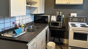 A compact kitchen with white cabinets, a microwave, a toaster, a coffee maker, and a stove.