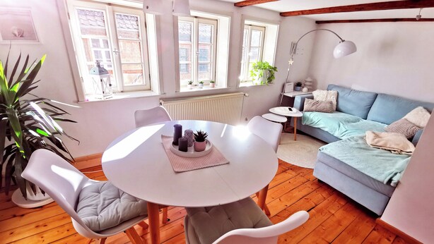 A cozy living room with a round table, two chairs, a blue sofa, and a wooden floor.
