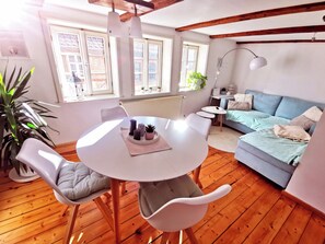 A cozy living room with a round table, two chairs, a blue sofa, and a wooden floor.