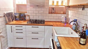 A kitchen with white cabinets, a wooden countertop, a gas stove, a sink, and a wine bottle.