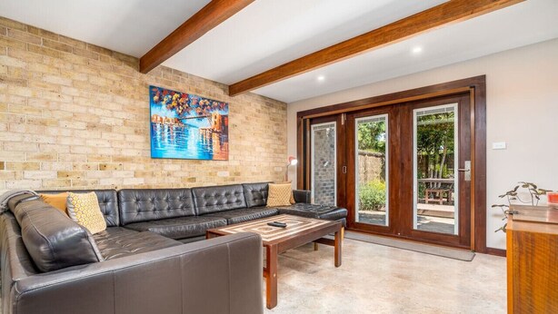 A living room with a black leather sofa, a wooden coffee table, and a painting on the brick wall. - Charming two-story 2BR townhouse in Braddon (Braddon)