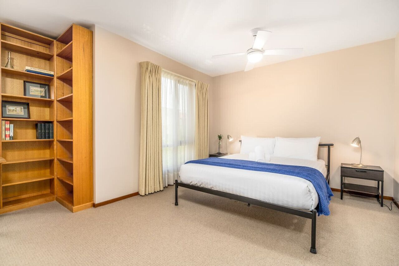 Un dormitorio con una cama, una estantería de madera, una mesita de noche y un ventilador de techo.
