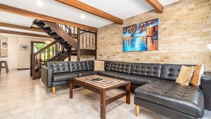 A spacious living room with a black leather sectional sofa, a wooden coffee table, and a staircase leading to another level. - Charming two-story 2BR townhouse in Braddon (Braddon)