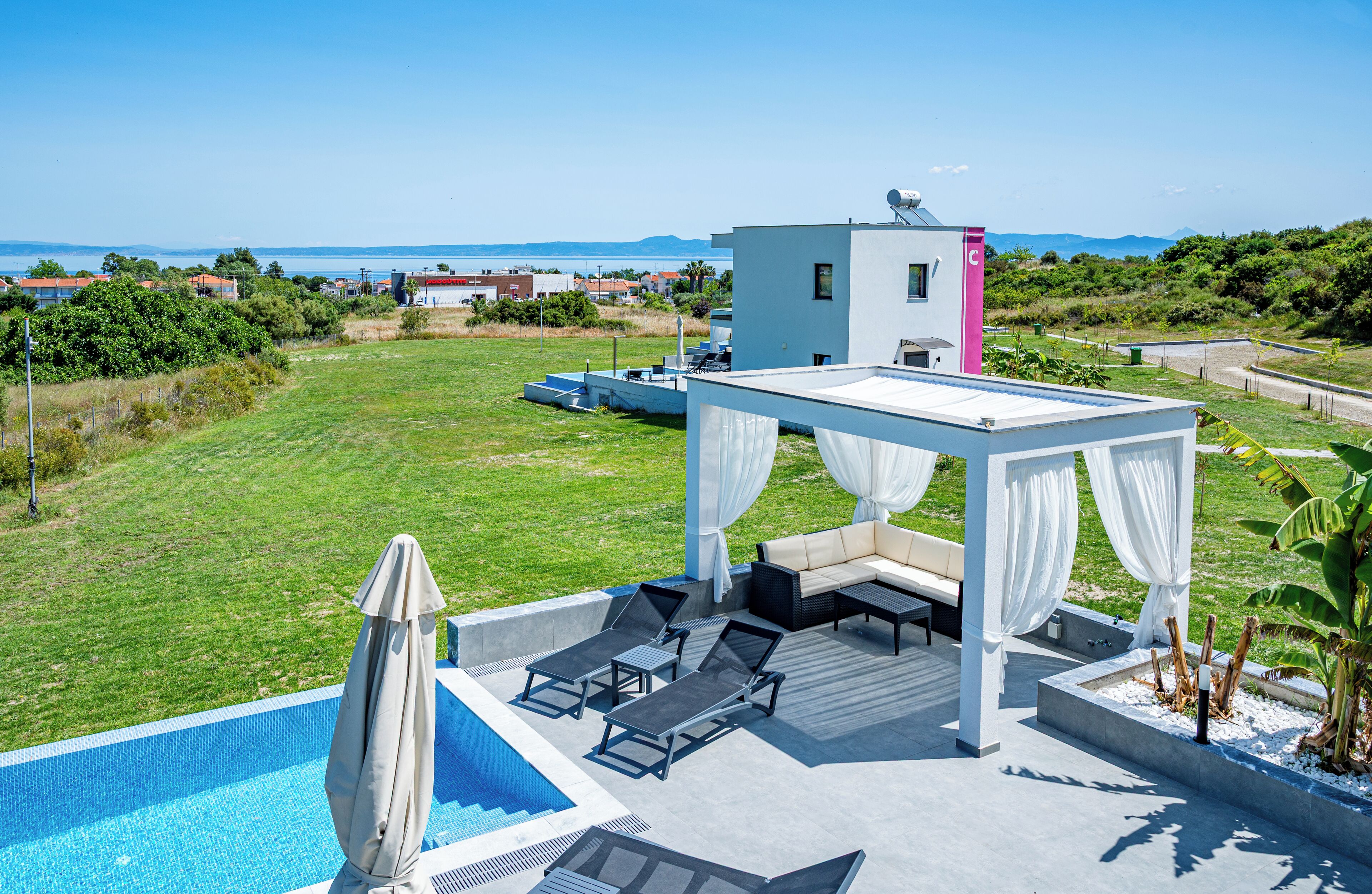 A rooftop pool area with a white gazebo, lounge chairs, and a view of the sea.