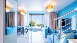 Un salon moderne avec un canapé bleu, un coin repas avec des chaises, un escalier et une grande fenêtre donnant sur l’extérieur.