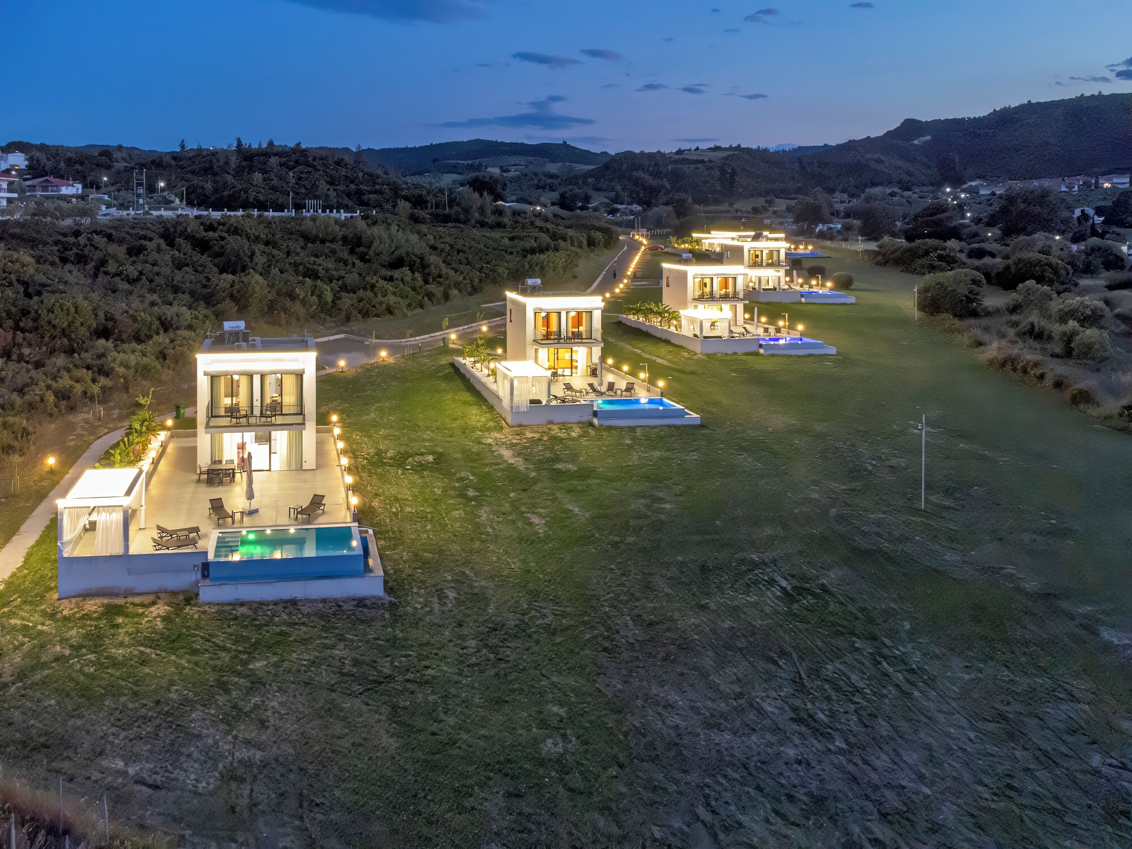 Ein modernes, mehrstöckiges Haus mit Swimmingpool, Sitzgelegenheiten im Freien und einer gut beleuchteten Auffahrt.