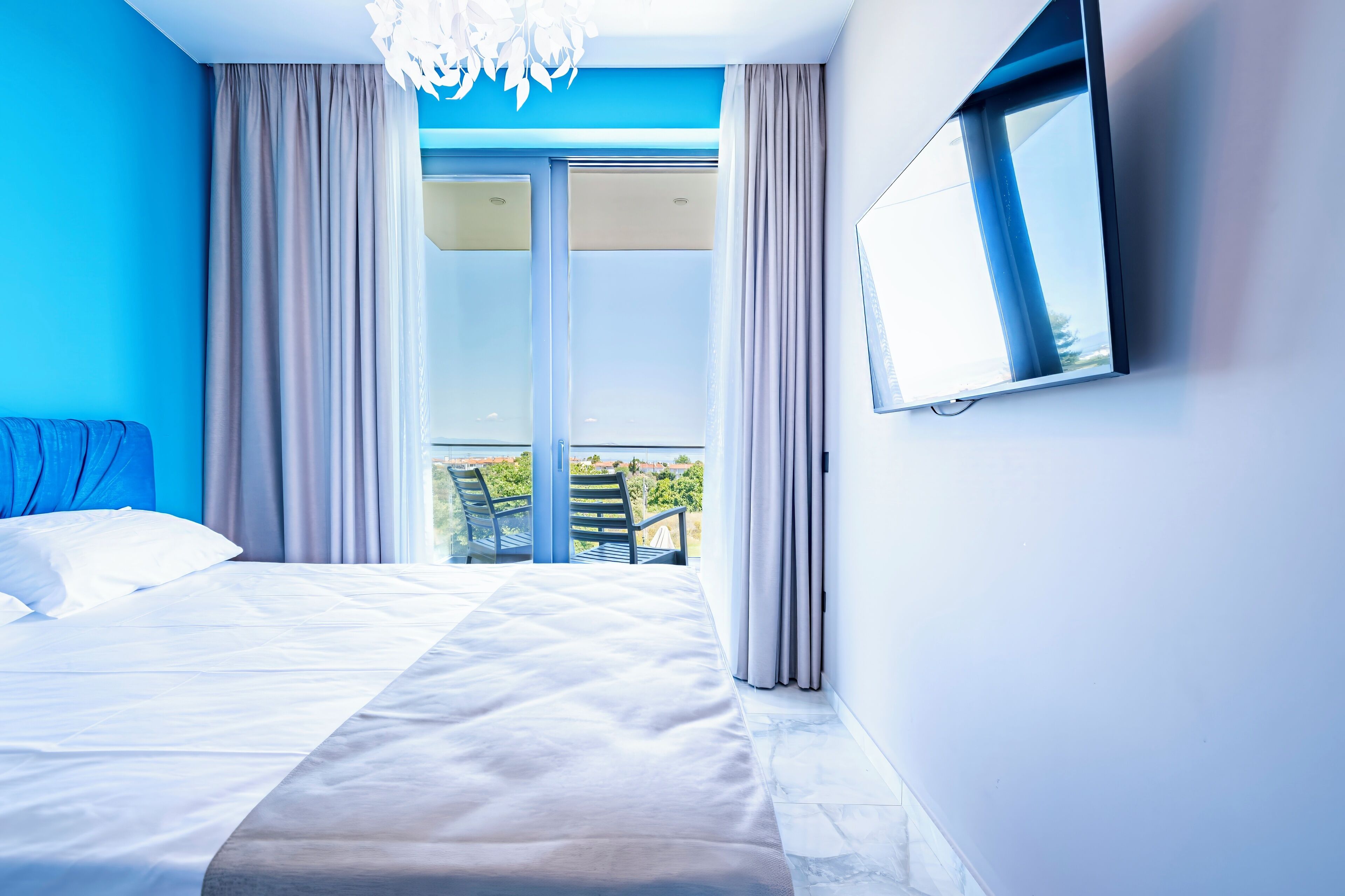 A hotel room with a bed, a TV mounted on the wall, and a balcony with a view.