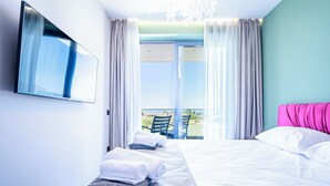 Une chambre d’hôtel avec un lit, un téléviseur fixé au mur, un balcon avec vue et une chaise.