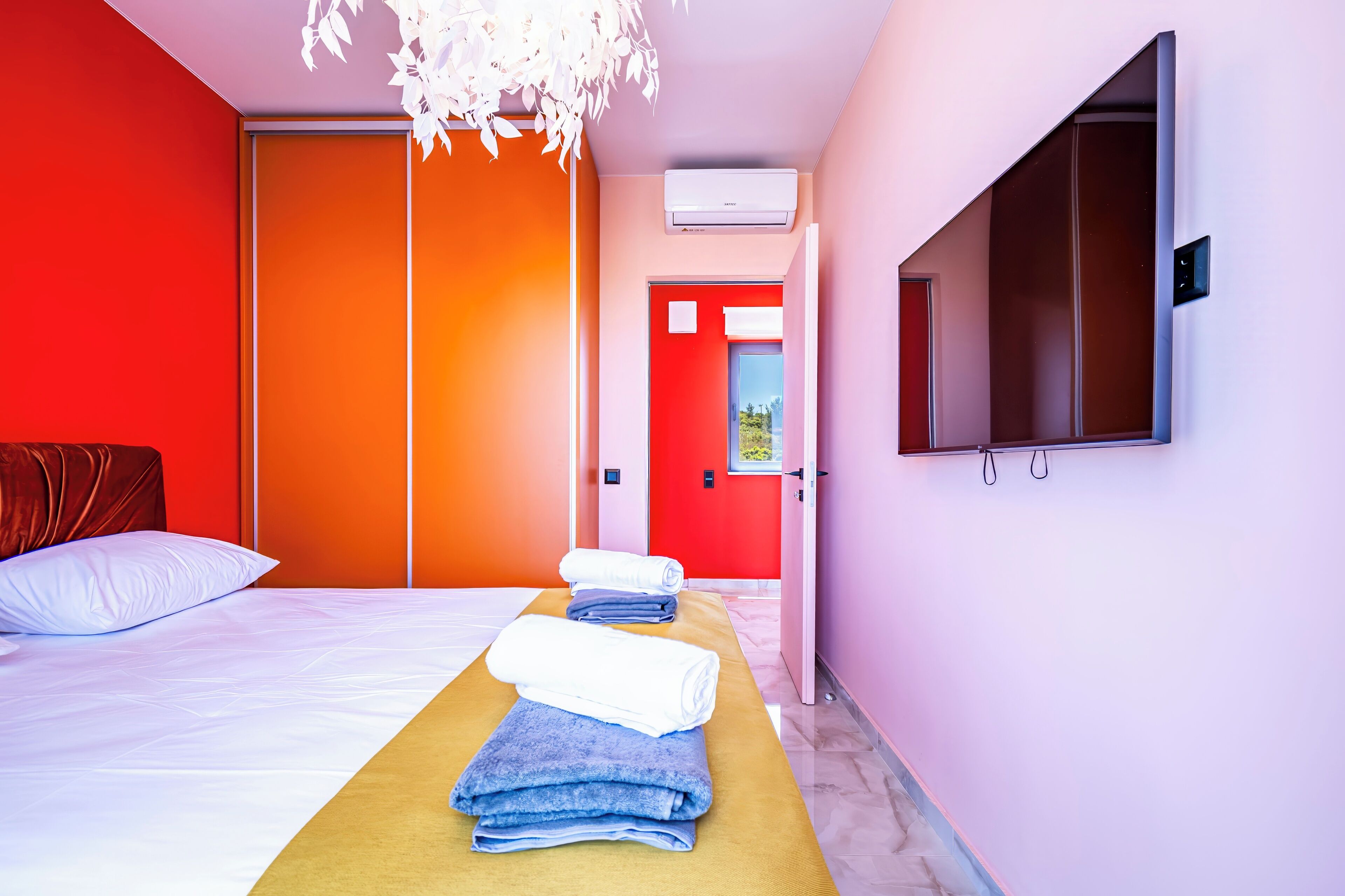 A hotel room with a bed, a massage table with towels, a TV, and an air conditioning unit.