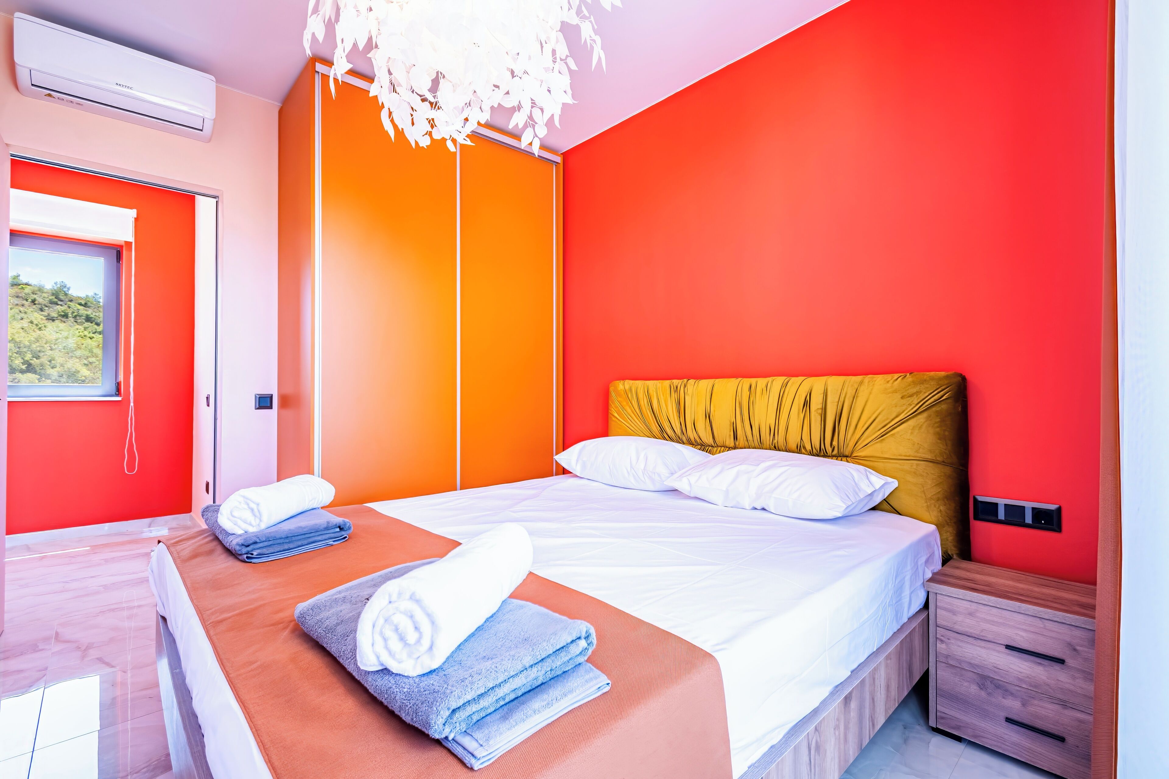 Une chambre d’hôtel moderne avec un mur d’accent rouge, un lit avec du linge de maison blanc et une table de chevet en bois.