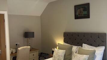 Um quarto com uma cama grande, cabeceira, escrivaninha com luminária e um quadro na parede.