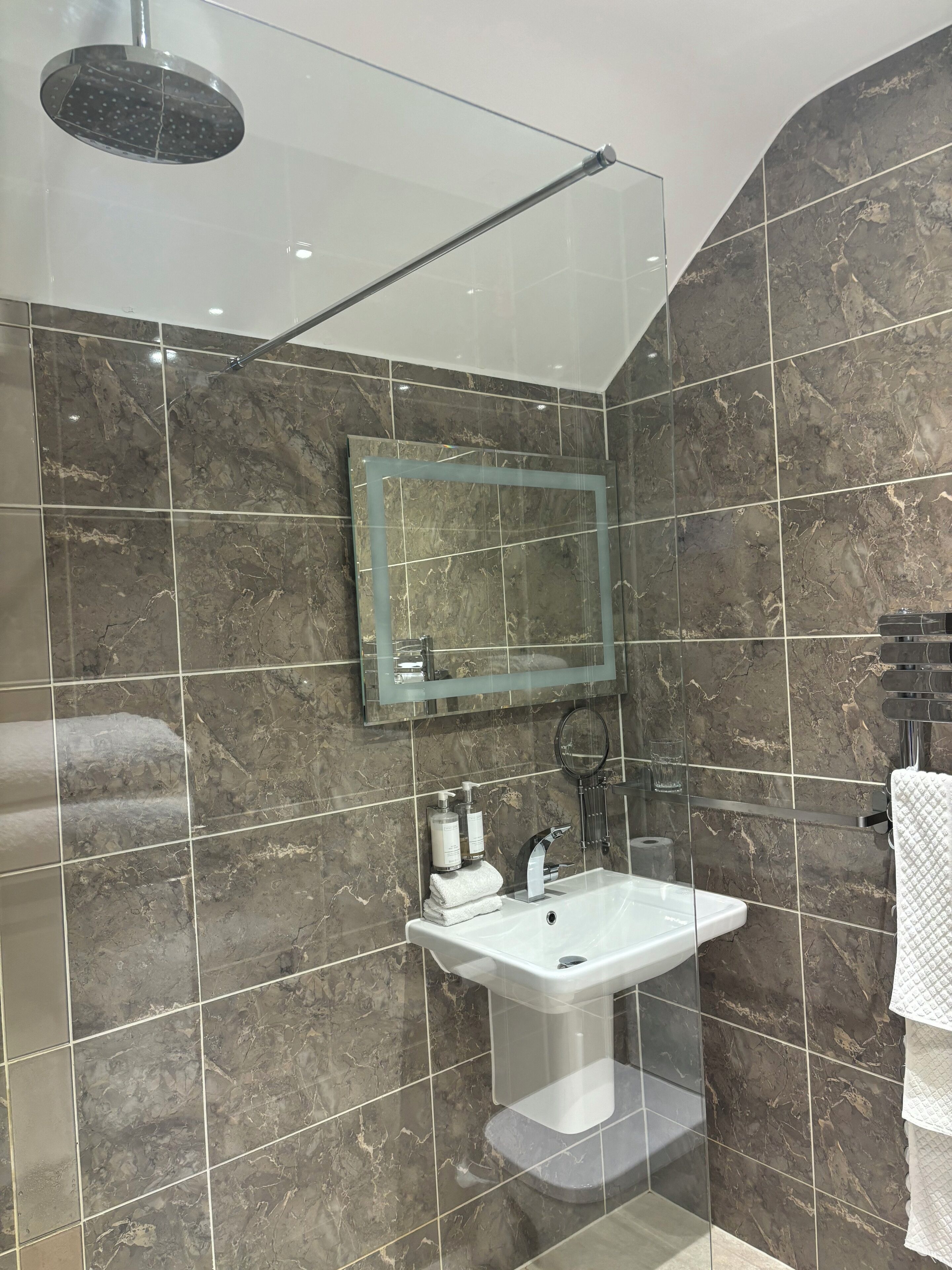 Un bagno moderno con doccia vetrata, parete rivestita in marmo, lavabo con specchio e porta asciugamani.