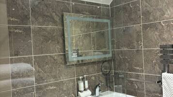 Un bagno moderno con doccia vetrata, parete rivestita in marmo, lavabo con specchio e porta asciugamani.
