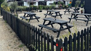 A rustic outdoor seating area with thatched-roof buildings, picnic tables, and umbrellas. - The Red Cow Inn (Royston)