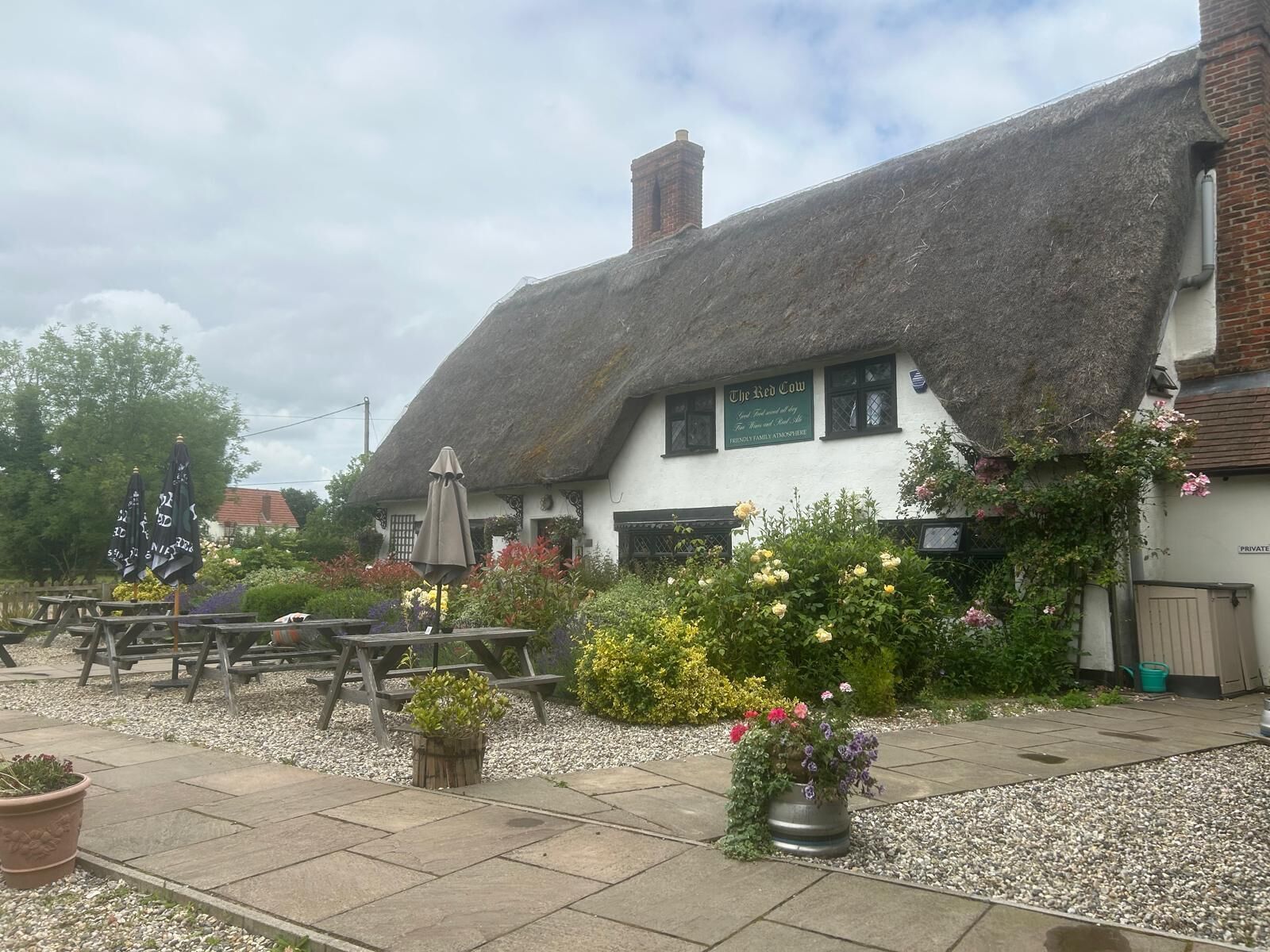 A traditional thatched-roof building with outdoor seating and flower beds.