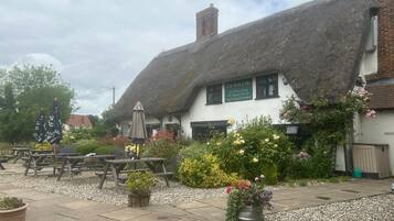 A traditional thatched-roof building with outdoor seating and flower beds.