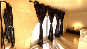 Una habitació amb un mirall gran, cortines negres, un llit i una tauleta de nit amb una làmpada.