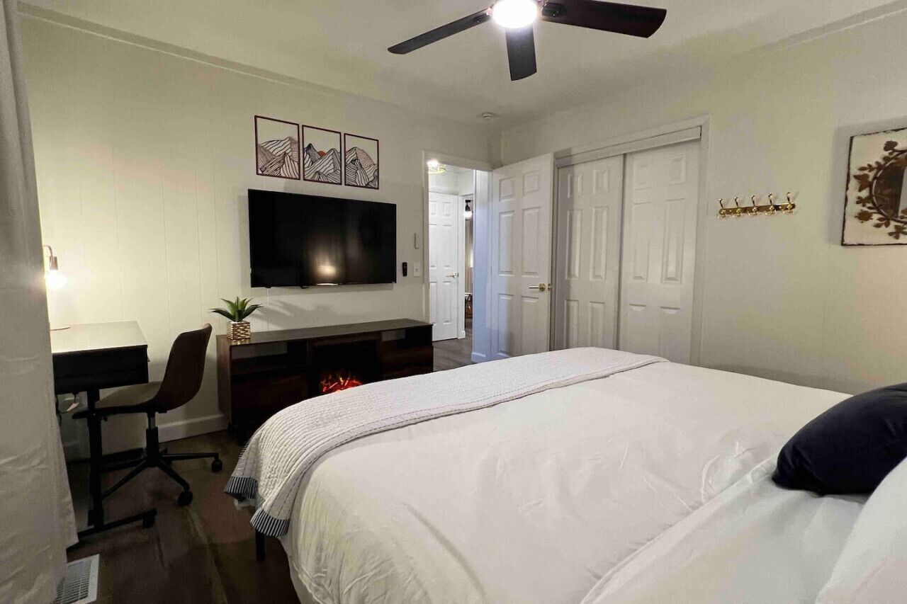 A hotel room with a bed, desk, chair, TV, and a ceiling fan.