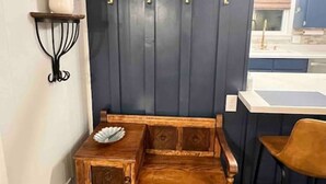 Une pièce d’angle avec un banc en bois, un meuble mural doté de plusieurs tiroirs, une petite table ornée d’un objet décoratif et une étagère murale sur laquelle est posée une plante.