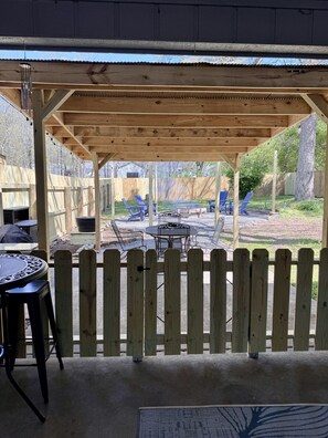 A covered patio area with a wooden fence, a table with chairs, and a view of the backyard. - Belle Maison, Heart of Greers Ferry Lake Area, Extended Stays Welcome (Greers Ferry)