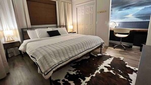 Une chambre à coucher comprenant un lit, un bureau, une chaise, un tapis en peau de vache, une tête de lit, des rideaux et une porte.