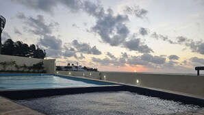 Ein Schwimmbecken mit Sonnenuntergangsblick, einer Betonplattform und einer entfernten K üstenlinie.