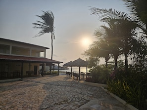 A courtyard with a stone floor, a building with a tiled roof, and a palm tree. - Malie Hotel (Cascavel)