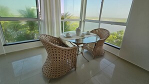 Ein Balkon mit einem Glastisch, zwei Korbstühlen und Blick auf das Meer.