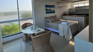 Ein modernes Zimmer mit großem Fenster, einem Esstisch mit Stühlen, einer Couch und einer Küchenzeile.