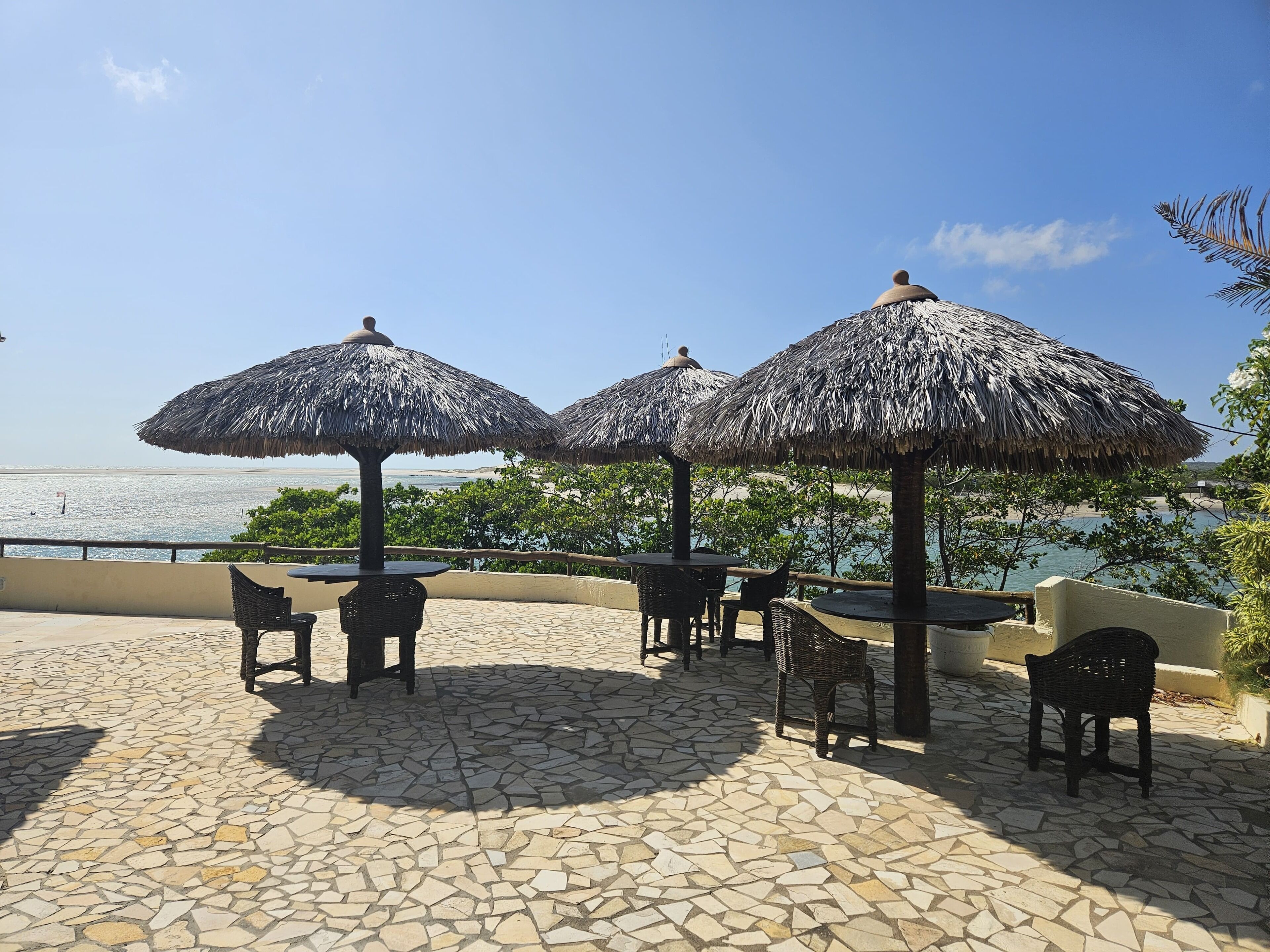 Een terras met rieten parasols, rieten meubels en uitzicht op zee.
