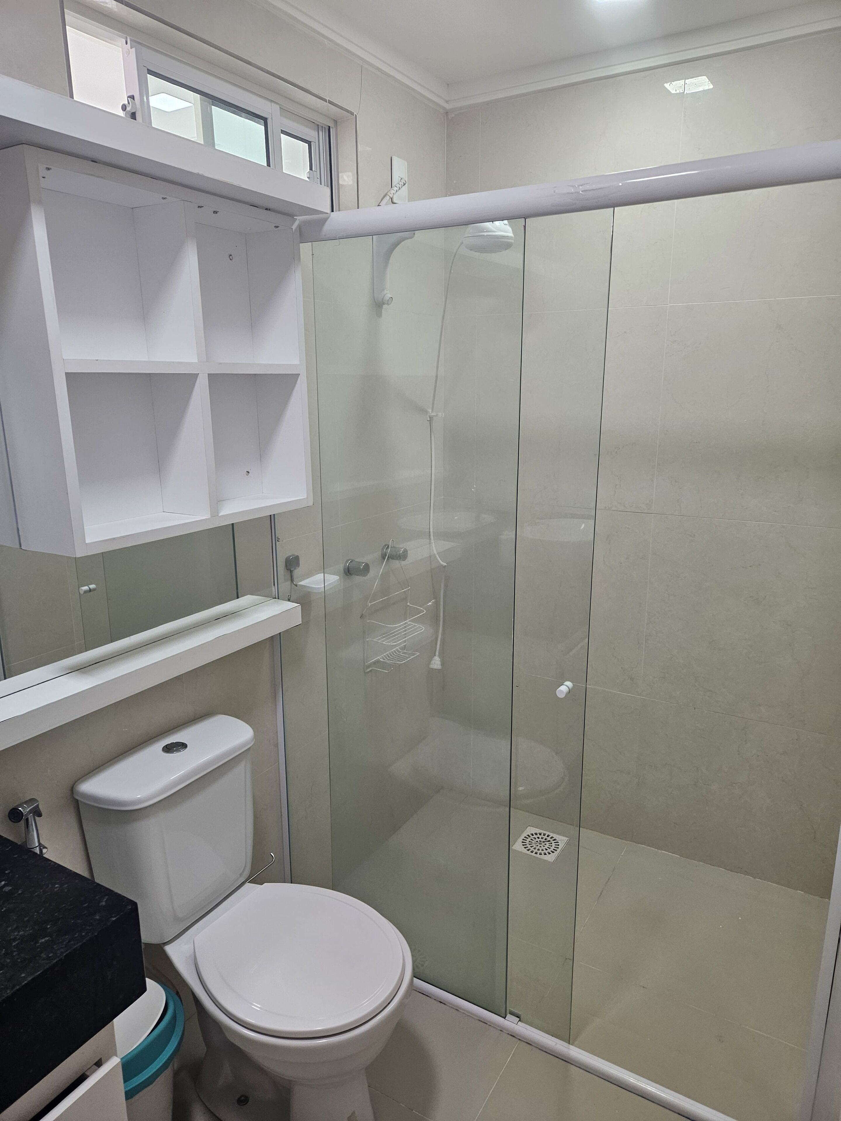 Casa de banho moderna com chuveiro envidraçado, sanita e lavatório branco.