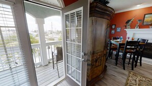 A room with a wooden floor, a dining table with chairs, a white door with glass panels, and a view of the outdoors through the door. - Seaside Serenity (Panama City Beach)
