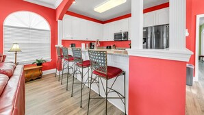 A modern kitchen with white cabinets, a red accent wall, and a bar area with wicker chairs. - Seaside Serenity (Panama City Beach)