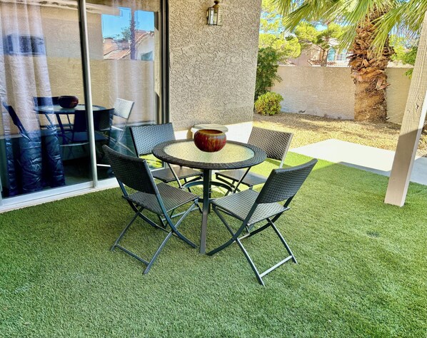 A patio with a round table and four chairs, surrounded by artificial grass.