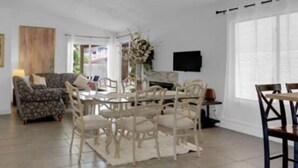 A spacious living room with a round table and chairs, a sofa, and a television on the wall.